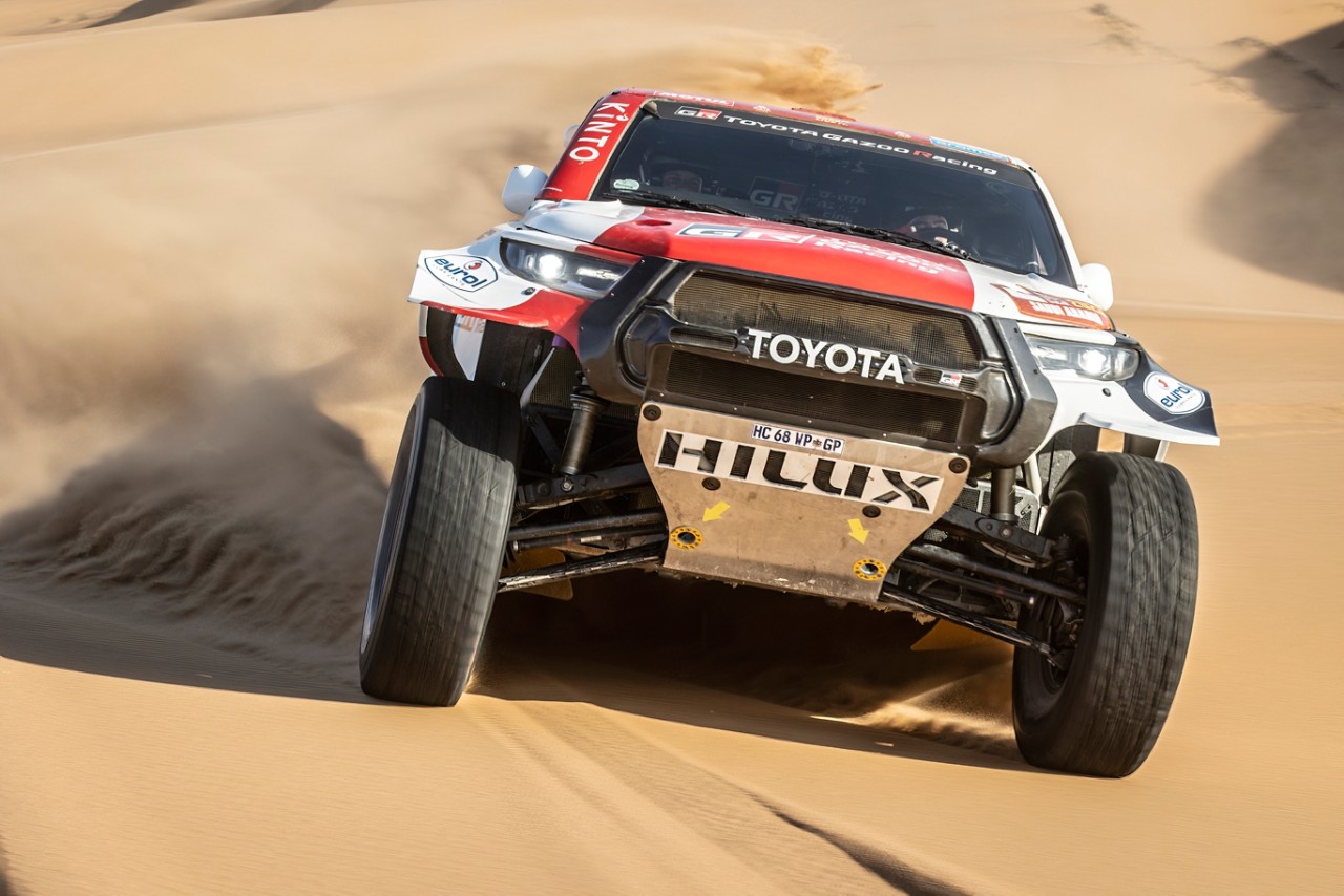 Low angle front on Hilux driving up desert dune