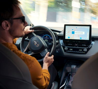 Un uomo con un maglione arancione si gira verso destra mentre guida un’auto Toyota. Sul display del sistema multimediale dell’auto è visualizzato un aggiornamento software.